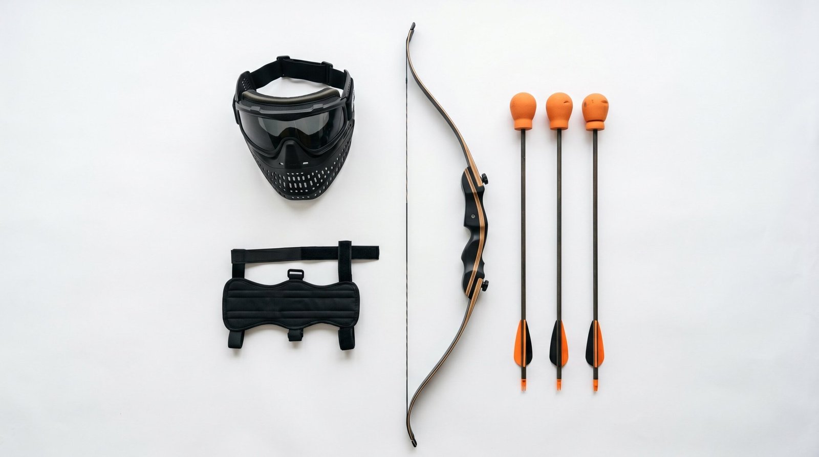 Archery tag equipment laid out including a recurve bow, foam-tipped safety arrows with large foam heads, a protective face mask, and a forearm arm guard